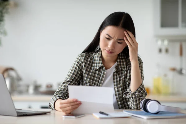 Verärgert asiatische Frau sitzt in Küche und liest Brief — Stockfoto