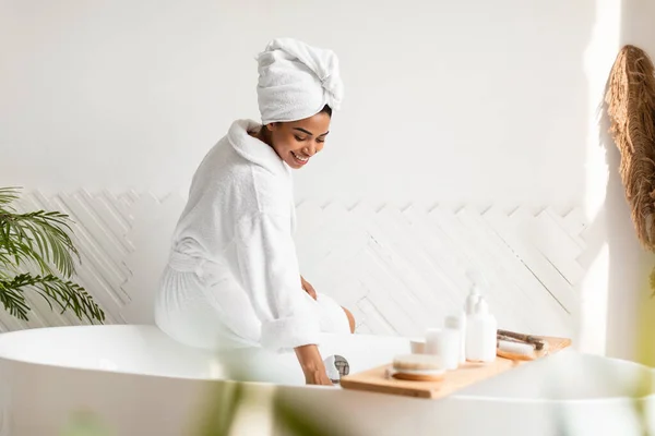 Feliz mulher afro-americana tocando água preparando banho em casa — Fotografia de Stock