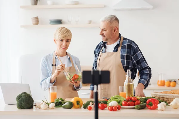 Çift birlikte yemek pişiriyor, yemek tarifi veriyor ve akıllı telefon kamerası ve tripodla vlog ve sosyal medya videoları kaydediyor.