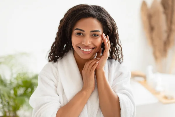 Afrikaanse vrouw aanraken gezicht glimlachen naar camera poseren in de badkamer — Stockfoto
