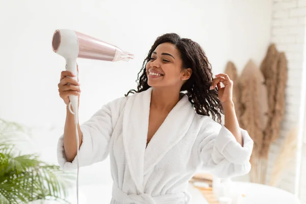 Happy Black Woman keriting keriting rambut dengan pengering rambut di kamar mandi — Stok Foto