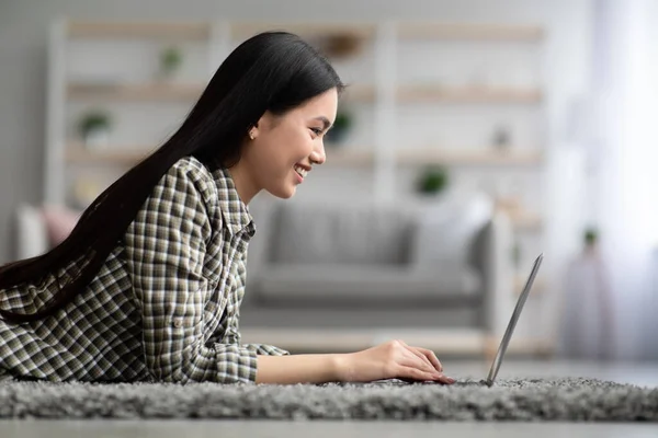 Side view van aziatische jonge vrouw met behulp van laptop thuis — Stockfoto