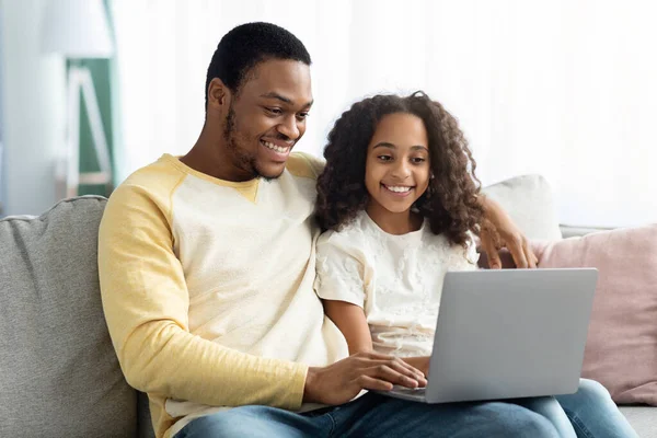 Fröhlich junger schwarzer Vater bringt seiner kleinen Tochter Laptop bei — Stockfoto