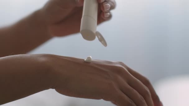 Close-up shot van onherkenbare zwarte dame knijpen crème uit buis op de hand en het toepassen van het, slow motion — Stockvideo