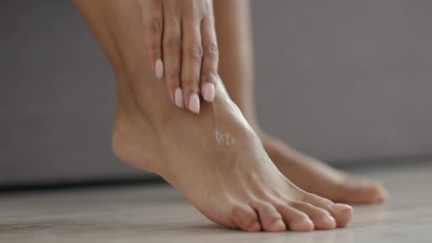 Fötterna försiktiga. Närbild skott av afrikansk amerikansk dam applicera fotkräm på hennes bara ben, njuter av behandlingsförfaranden — Stockvideo
