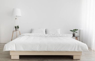 Yatak odasının içinde hafif minimalist tasarım. Beyaz yastıklı çift kişilik yatak ve battaniye, lamba, beyaz duvar, kopyalama alanı