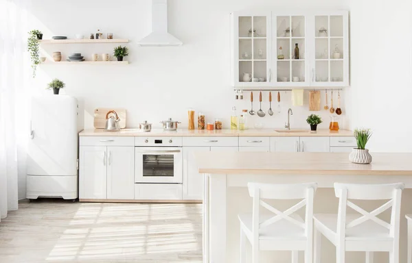 Light kitchen furniture after renovation. Kitchenware and plants on shelves, chairs and table in scandinavian style