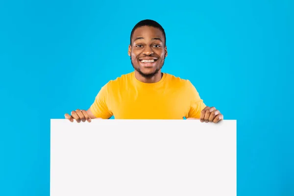 Czarny facet trzyma pustą tablicę białą księgę na niebieskim tle — Zdjęcie stockowe