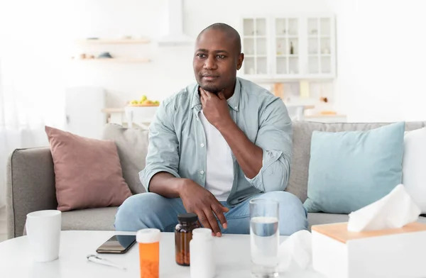 Érett afro-amerikai férfi hányinger, szenved torokfájás, ül a kanapén közel asztal szalvéták és tabletták — Stock Fotó