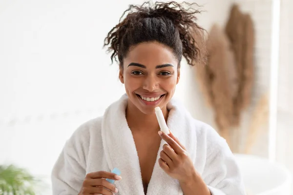 Señora africana aplicando bálsamo labial sonriendo a la cámara en el baño — Foto de Stock