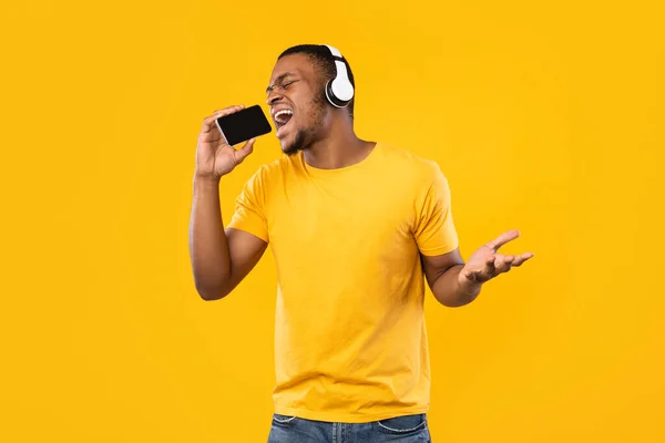 Hombre africano cantando sosteniendo Smartphone como micrófono usando auriculares, estudio —  Fotos de Stock