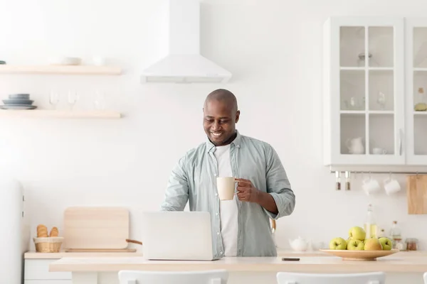 Kendini izole eden modern bir işçi. Kahve içen ve dizüstü bilgisayarla çalışan mutlu Afro-Amerikan adam. — Stok fotoğraf