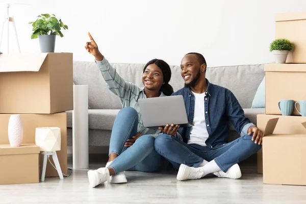 Smiling African Spouses Sitting With Laptop In New Flat And Pointing Away — Stock Photo, Image