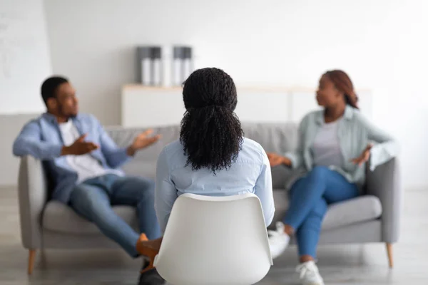 Marital therapy. Psychologist sitting with her back to camera during appointment with unhappy black couple at office