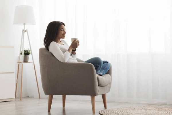 Está na hora de relaxar. Africano senhora americana sentado em poltrona com xícara de café e sonhando, desfrutando de manhã, espaço vazio — Fotografia de Stock