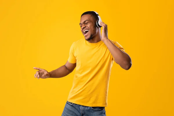 Homem Africano engraçado cantando e dançando usando fones de ouvido, fundo amarelo — Fotografia de Stock