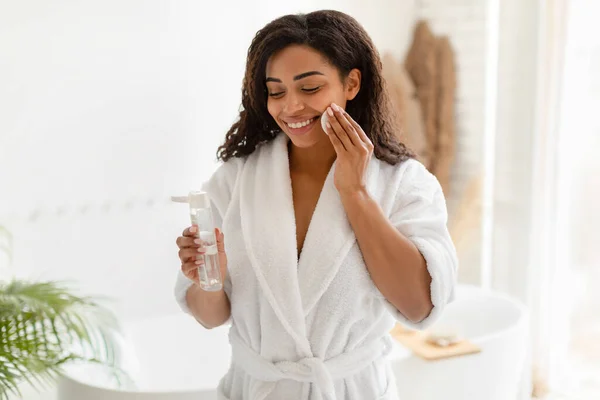 Mujer negra usando almohadilla de algodón y agua micelar en el baño — Foto de Stock