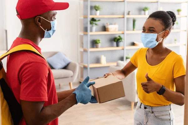 Schwarzer Kurier und weibliche Kundin gestikulieren Daumen hoch und tragen Masken im Haus — Stockfoto