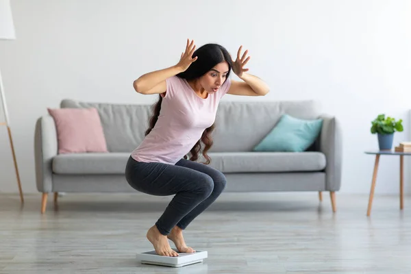 Emotionale Inderin mit Angst vor Übergewicht, die zu Hause schockiert auf einer Waage sitzt, kopiert den Raum. Gesunder Lebensstil — Stockfoto