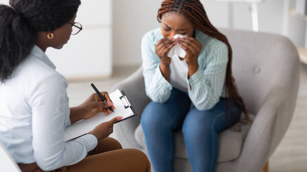 Unhappy black young woman crying at psychologists office, panorama