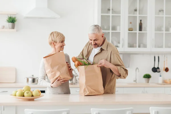 Senior par anländer från matvaror med eco bag, packa upp i köket — Stockfoto