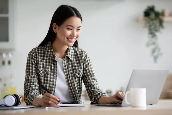 Lachende aziatische vrouw student met behulp van laptop voor het studeren thuis — Stockfoto