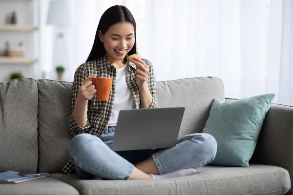Happy asian lady drinking tea while watching movies online