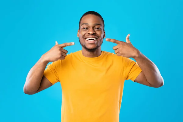 Nero uomo puntando dita al suo sorriso su sfondo blu — Foto Stock