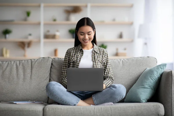 Sorrindo asiático mulher digitando no teclado laptop, casa interior — Fotografia de Stock