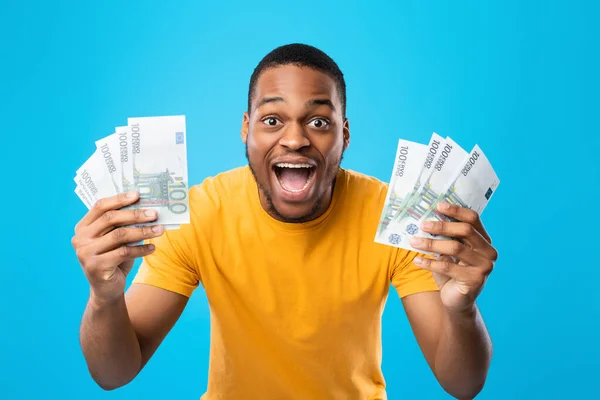 Cara preto mostrando euro dinheiro gritando em alegria, fundo azul — Fotografia de Stock