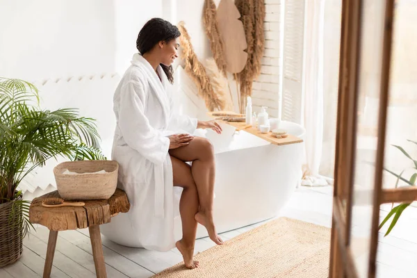 Zwart vrouw voorbereiding bad toevoegen badzout zitten in de badkamer — Stockfoto