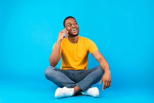 Alegre preto homem falando no celular sentado sobre azul fundo — Fotografia de Stock