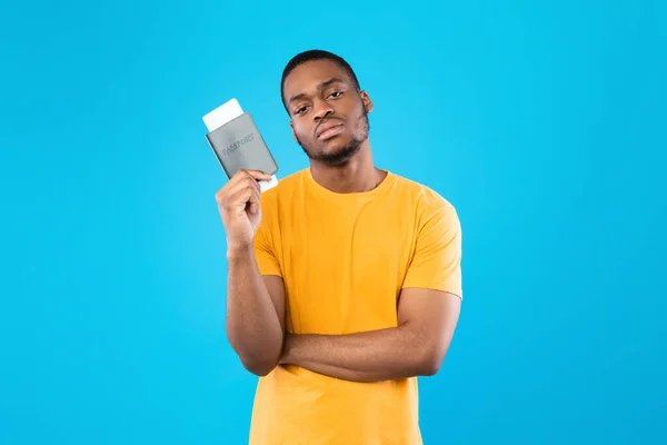 Descontento hombre de turismo negro sosteniendo boletos de viaje sobre fondo azul —  Fotos de Stock