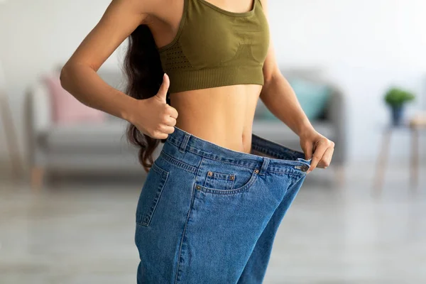 Close-up de jovem indiana senhora em jeans grandes mostrando polegar para cima, recomendando seu programa de perda de peso, vista cortada — Fotografia de Stock