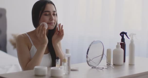 Cuidados domésticos com a pele. Jovem senhora oriental limpando seu rosto com loção e almofadas de algodão, preparando-se para a maquiagem diária — Vídeo de Stock