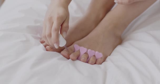 Female beauty routine concept. Unrecognizable lady making pedicure sitting in bed at home, applying pink polish — Stock Video