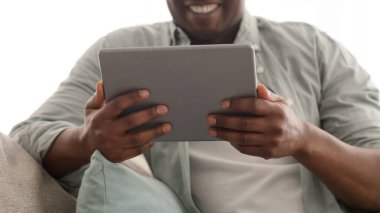 Boş zamanların modern teknolojileri. Siyah olgun bir adam dijital tablet kullanıyor, internette sörf yapıyor ya da video görüşmesi yapıyor.