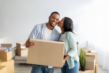 Mutlu kadın kocasını yanağından öpüyor, karton kutu tutuyor, yeni eve taşındıktan sonra eşyalarını açıyor.