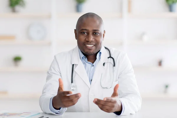 Afrikalı Amerikalı doktor klinikteki çalışma masasında oturuyor, koronavirüs salgını sırasında randevuları var. — Stok fotoğraf