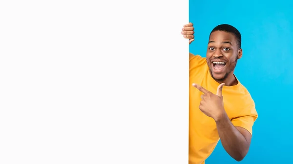 Homem Africano excitado apontando o dedo no cartaz de papel, fundo azul — Fotografia de Stock