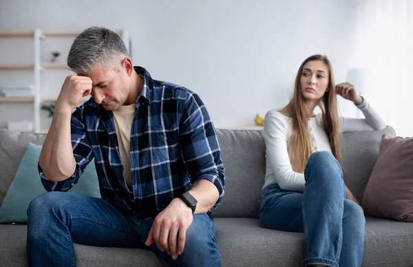 Depressiver älterer Mann sitzt auf Couch, tief in Gedanken nach Streit mit Freundin, beleidigte Dame schaut ihn an — Stockfoto