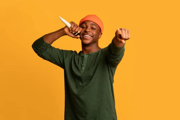 Joyful jovem negro cantando com microfone e apontando para a câmera — Fotografia de Stock