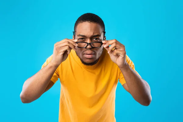 Uomo afroamericano che strizza gli occhi guardando attraverso gli occhiali, sfondo blu — Foto Stock