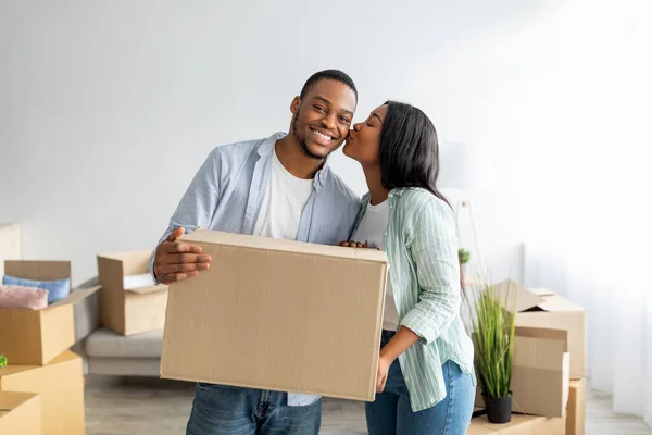 Happy woman kissing husband in cheek, holding paper boxes, unpacking stuff after relocationg to new house — Stock Photo, Image