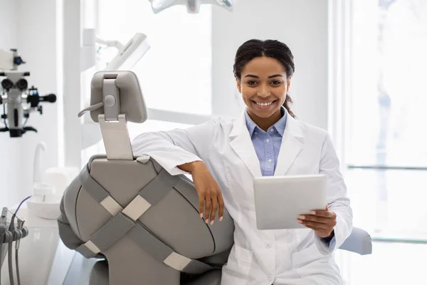 Donna dentista nera felice con la compressa digitale che posa sul posto di lavoro in clinica — Foto Stock