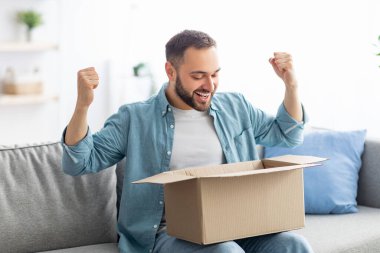Tatmin olmuş erkek müşteri kutusunu açıyor, teslimat için heyecanlanıyor, online mağaza siparişi alıyor, evde EVET işareti yapıyor.