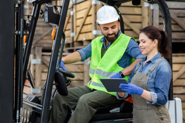Milenyum sakallı adam forklift kamyonunda gülümseyen bir kadınla düzeni tartışıyor.