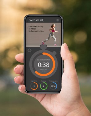 Cep telefonunda fitness uygulaması kullanan, dışarıda ticaret yapan bir kadın.