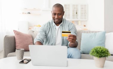Kolay ödeme ve nakit ödeme konsepti. Mutlu Afrikalı Amerikalı adam kredi kartı tutuyor ve dizüstü bilgisayar kullanıyor.