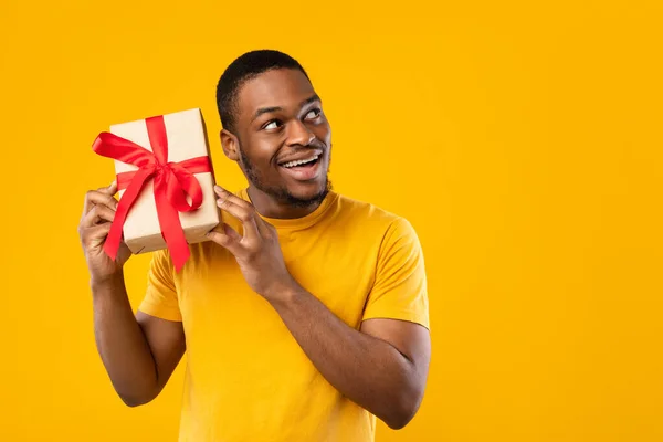 Grappig Afrikaans Guy Holding Gift raden wat er binnen, gele achtergrond — Stockfoto